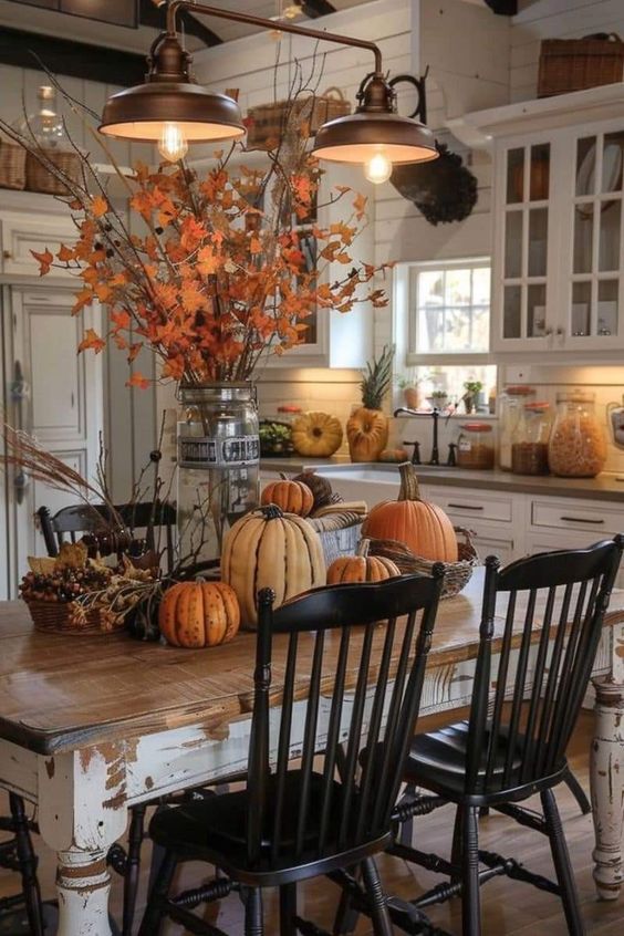 Stepping into this cozy kitchen, you’re instantly greeted by the warm, inviting vibes of fall! The rustic wooden table is adorned with an array of pumpkins in various shapes and sizes, perfectly capturing the essence of autumn. The centerpiece is a tall glass jar filled with vibrant orange leaves, adding a touch of nature indoors. Overhead, the vintage-style pendant lights cast a soft, warm glow, making this space feel even more welcoming. It’s the perfect spot for a pumpkin spice latte on a crisp fall morning!