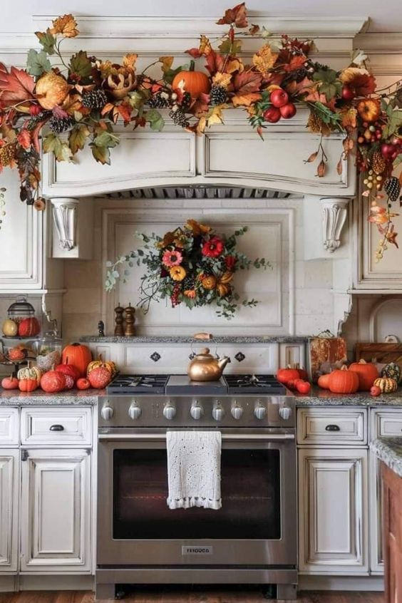 This kitchen has been transformed into a fall wonderland! The area above the stove is adorned with a lush garland bursting with vibrant autumn leaves, pumpkins, pinecones, and berries, bringing the warm colors of the season right into the heart of the home. Below, the stovetop is flanked by an array of pumpkins and gourds in various shapes and sizes, adding a festive touch to the countertops. A beautiful wreath filled with sunflowers and greenery hangs above the range, tying the whole look together. The soft, neutral tones of the cabinetry provide the perfect backdrop, allowing the rich fall colors to truly pop. This kitchen is ready to welcome the season in style!