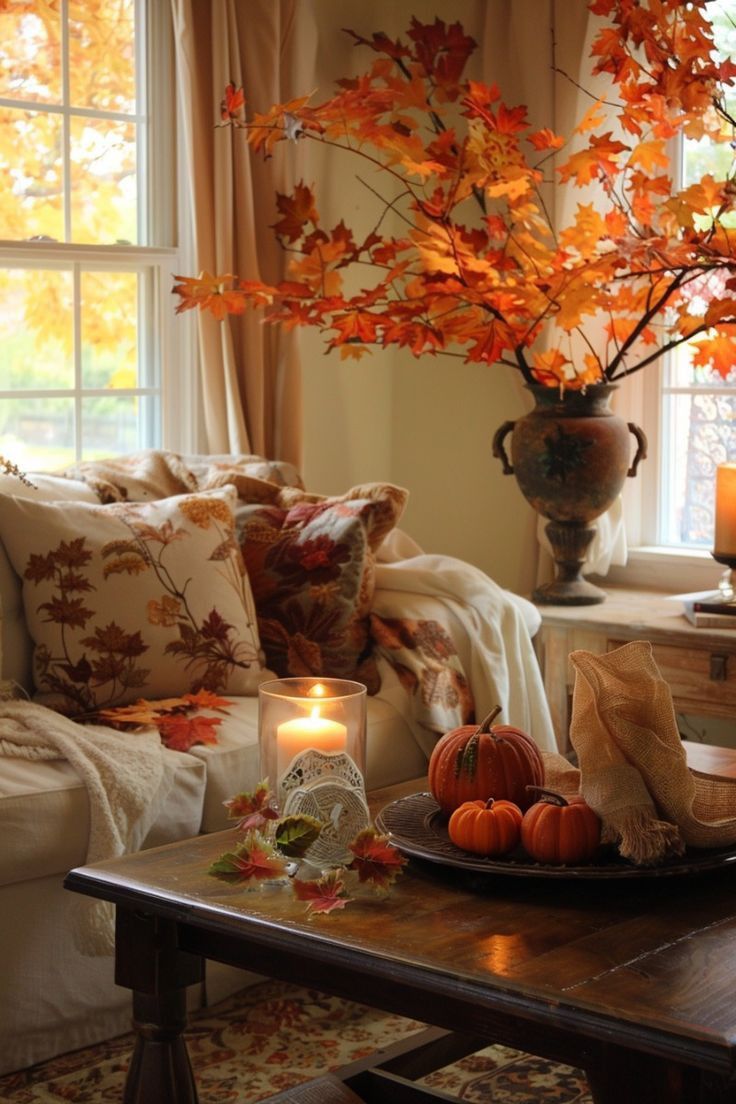 This living room corner exudes cozy autumnal vibes, perfect for relaxing as the leaves fall outside. The soft beige sofa is adorned with pillows featuring rich leaf patterns, adding a touch of fall's natural beauty to the space. A throw blanket casually draped over the armrest invites you to snuggle up and enjoy the season. On the coffee table, a simple yet elegant arrangement of small pumpkins sits beside a flickering candle, casting a warm, inviting glow. The highlight is the large vase filled with vibrant orange and red maple branches, which brings a burst of autumn color indoors, complementing the golden leaves visible through the window. This setup creates a serene and welcoming atmosphere, ideal for savoring the comforts of home during the fall season.