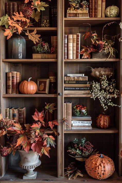 This bookshelf is a beautiful blend of literature and fall decor, creating a cozy and stylish corner perfect for the season. The shelves are filled with a mix of vintage books and autumnal accents, including small pumpkins, clusters of berries, and lush fall foliage. The earthy tones of the wood and the warm colors of the leaves and pumpkins complement each other perfectly, adding depth and texture to the display. A large urn filled with vibrant leaves and berries adds a dramatic touch to the bottom shelf, while the top shelves feature elegant vases and decorative gourds that bring a touch of sophistication to the overall look. This setup is a perfect way to bring the beauty of fall indoors, combining the warmth of the season with the timeless charm of a well-curated bookshelf.