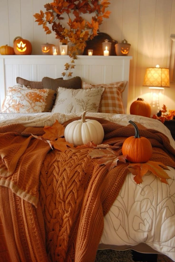 This bedroom is the ultimate cozy retreat, perfect for welcoming the fall season. The bed is layered with warm, textured blankets in rich autumn tones, creating an inviting place to snuggle up as the temperatures drop. A few small pumpkins, both white and orange, rest on the bed, adding a festive touch that ties in beautifully with the fall theme. The headboard shelf is adorned with a charming collection of carved pumpkins and glowing candles, casting a soft, warm light across the room. The backdrop of fall leaves and nature-inspired pillows completes the look, making this bedroom a perfect blend of comfort and seasonal charm.