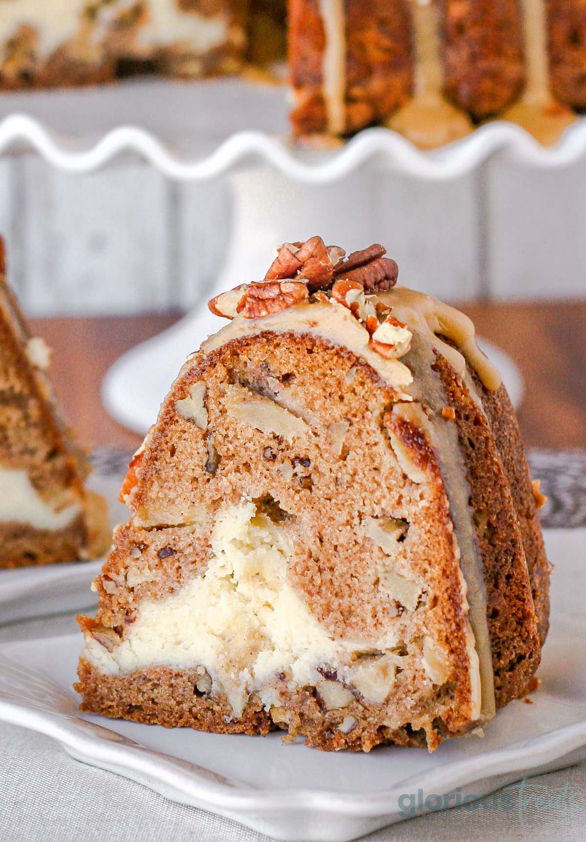 slice of apple bundt cake on a white square plate. you can see the cheesecake filling and praline frosting on top of the cake.