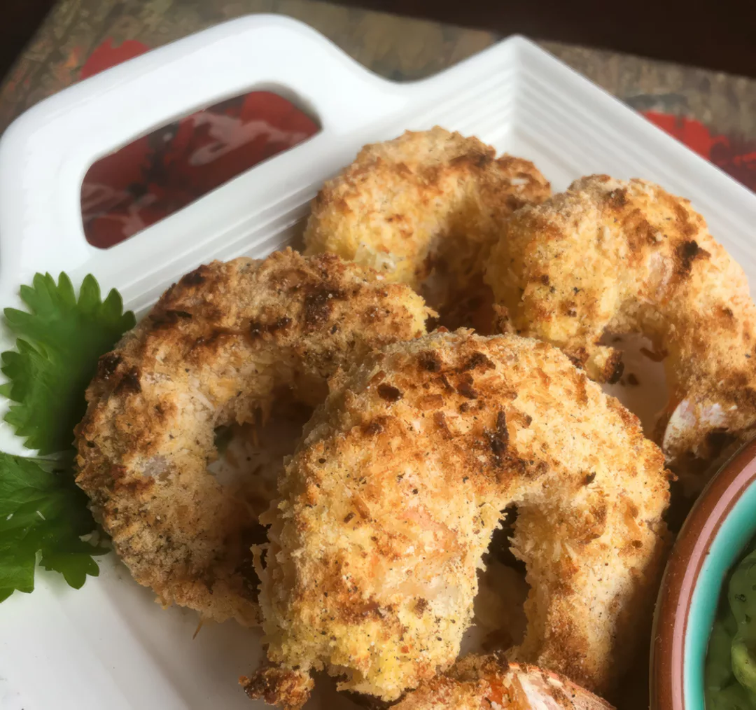 In traditional versions of this recipe, shrimp is coated with sweetened coconut flakes and panko breadcrumbs, then deep fried. This healthier, lighter version is gluten-free and baked, rather than fried. This version also calls for unsweetened coconut flakes, which allows the other seasonings to take center stage. Here, a tangy avocado-lime dip rounds out the flavors. However, a sugar-free orange marmalade would be a wonderful addition, as well.