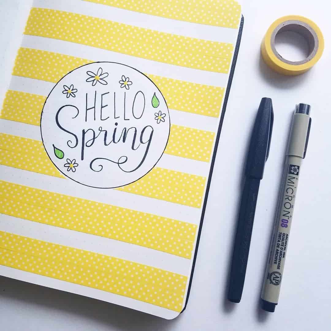 A photo of a Bullet Journal cover page that says Hello Spring with yellow washi tape in stripes for the background