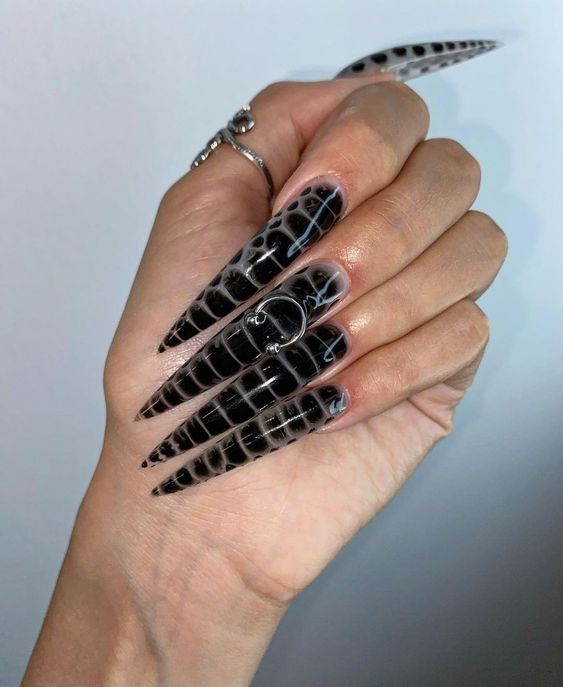 These stiletto nails feature a chic black and clear snake skin design, accented by a bold silver ring piercing for added drama. The glossy finish highlights the intricate pattern, creating a sophisticated yet edgy look perfect for making a statement.