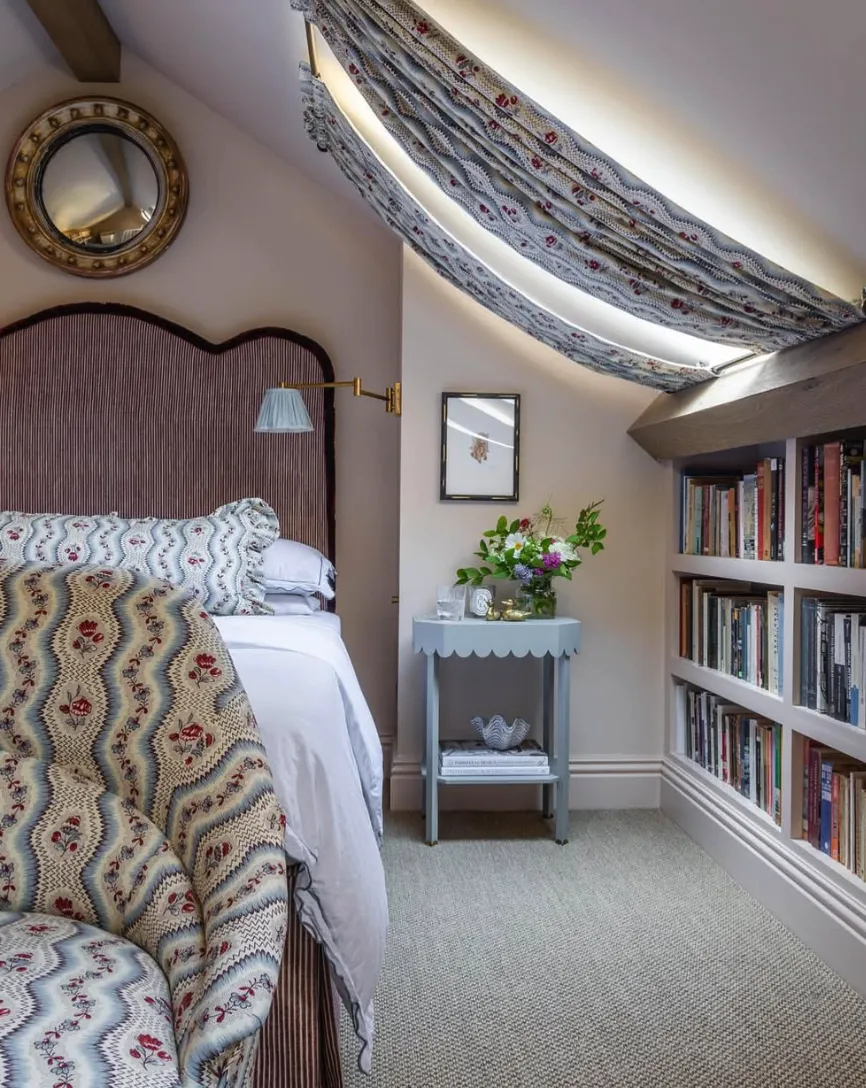 Charming Reading NookPerfectly blending functionality with coziness, this space features a built-in bookcase and patterned drapery to highlight the sloped ceiling. The scalloped nightstand and vintage-inspired mirror complete the look, creating an inviting retreat for book lovers.