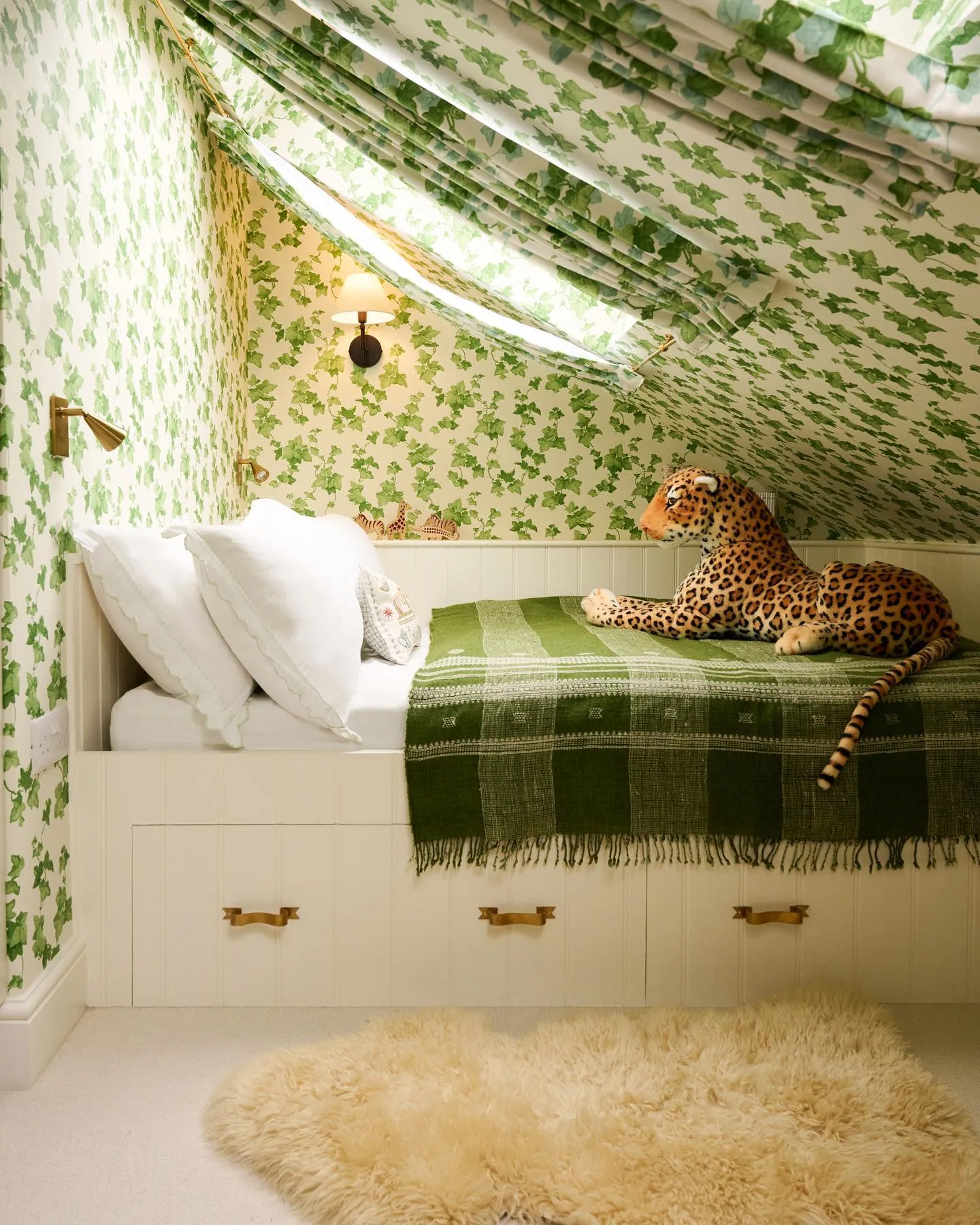 Whimsical GreeneryA leafy wallpaper and matching curtains create a magical garden-inspired vibe in this cozy attic room. The built-in bed with storage drawers and brass accents brings both charm and practicality to the small space.