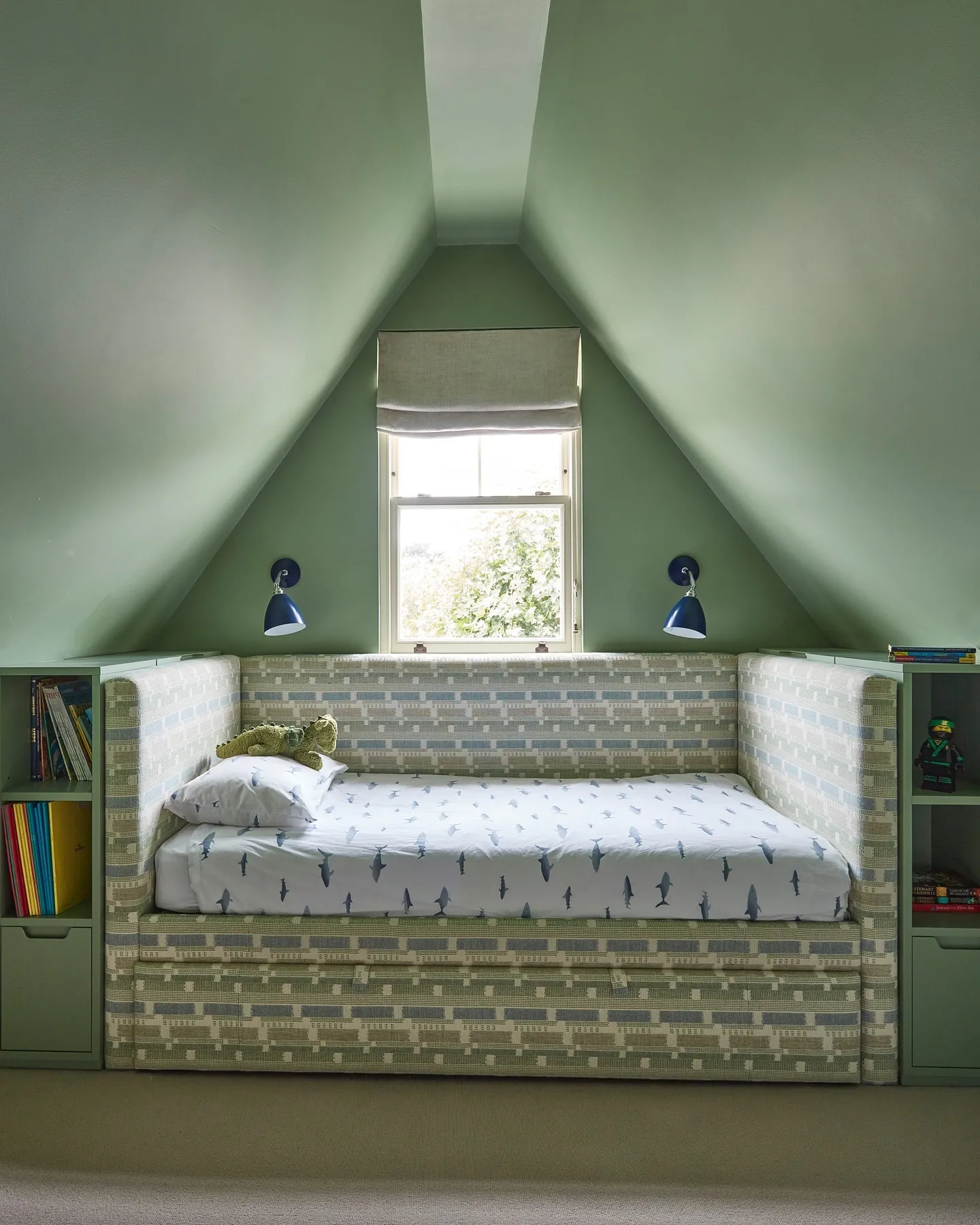 Sleek and Built-In ComfortThis attic bedroom maximizes its unique layout with a built-in daybed surrounded by shelves for books and toys. The soft green tones give the space a calming atmosphere, while the compact design makes it perfect for small spaces.