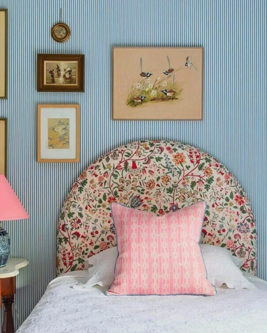 Delicate Florals with StripesA curved headboard upholstered in a vibrant floral pattern introduces a soft, vintage vibe to the space. Paired with the striped blue wallpaper and pastel accents, it exudes charm. This DIY project might require cutting a custom foam base to match the curved design before attaching the fabric. While it's manageable at home, seeking help for a polished finish on intricate curves is advisable.