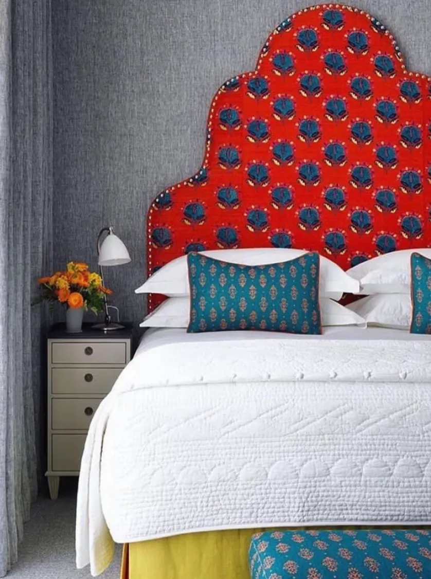 Bold and Whimsical RedThe rich red fabric headboard with intricate floral motifs makes a bold statement against a neutral textured wall. It introduces a mix of modern and classic styles while complementing blue-patterned pillows and bedding. Upholstering a headboard with such a unique fabric may require a trip to a specialty fabric store. It's a great project for those confident with DIY, but a professional can guarantee crisp edges and secure fabric folds.