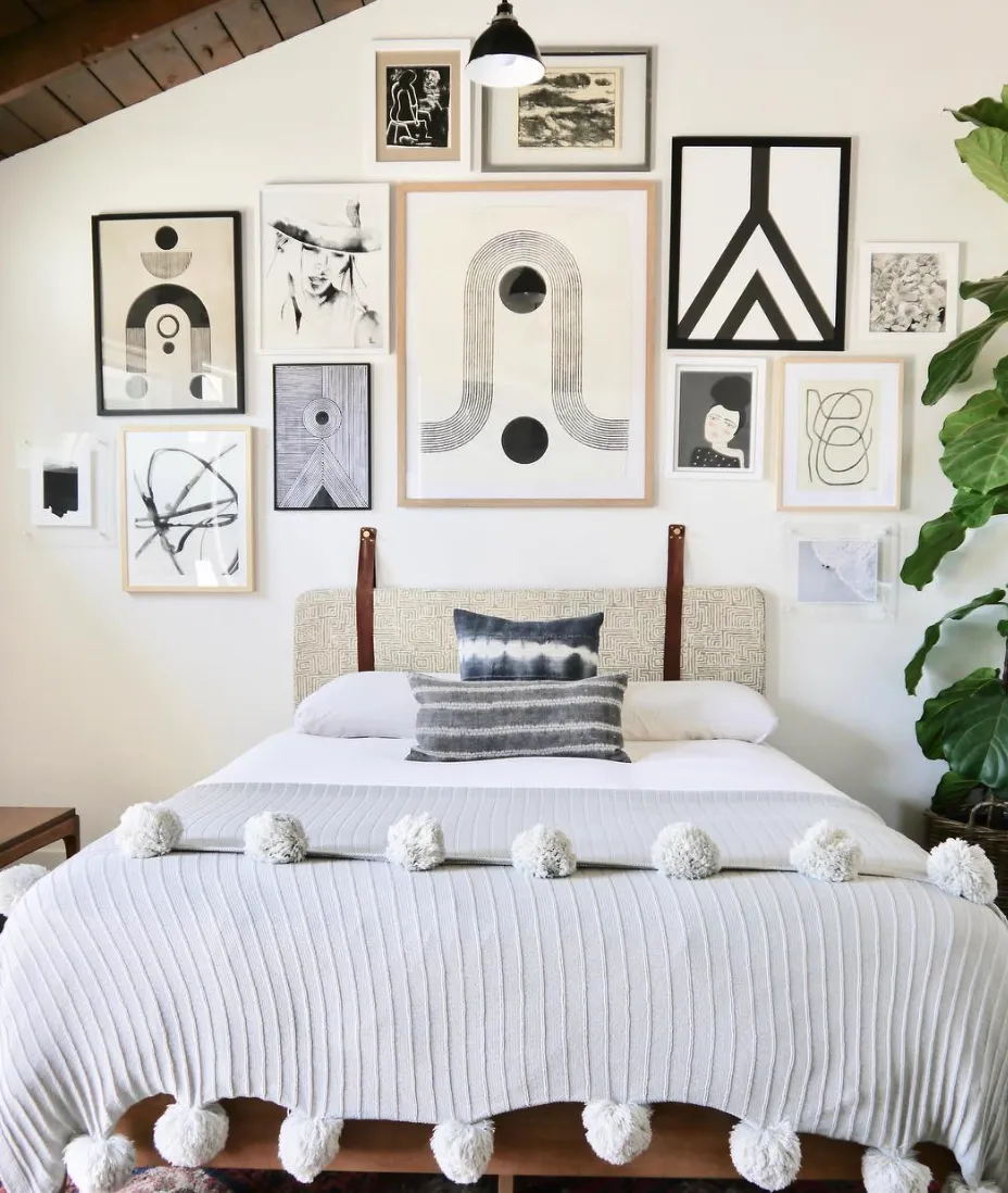 Modern Monochrome Gallery WallA chic monochrome gallery wall dominates this serene bedroom. The combination of abstract art, line drawings, and minimal photography offers a modern aesthetic. Black-and-white tones contrast beautifully with the warm wood elements and textured textiles. The pom-pom blanket adds a playful touch to the otherwise sophisticated decor. This design works wonderfully for minimalists looking to add character without overwhelming the space.