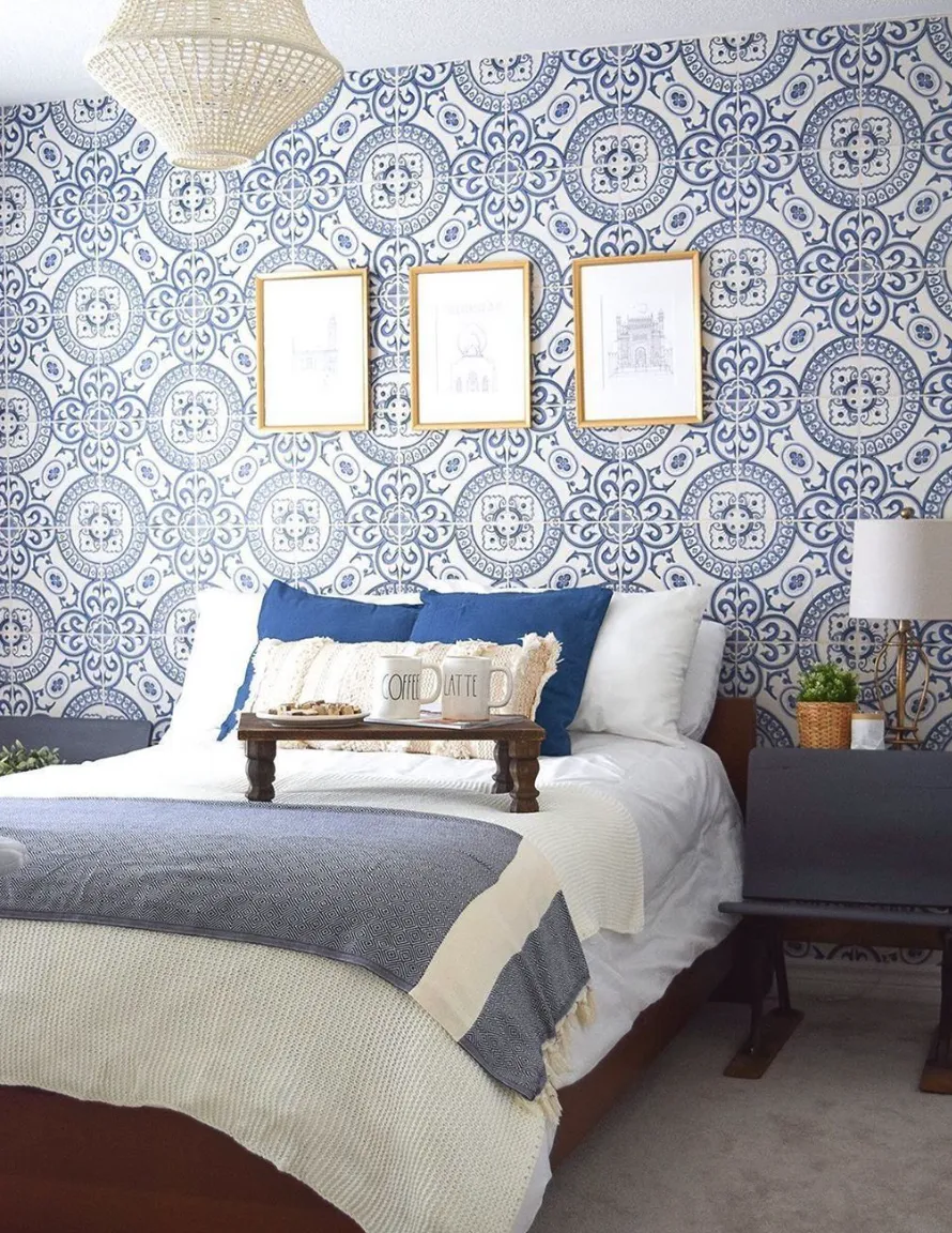 A charming, coastal-inspired bedroom features a patterned blue-and-white tile accent wall that serves as a fresh and inviting focal point. The tiles resemble intricate Mediterranean or Moroccan motifs, giving the space a vibrant, breezy vibe. This effect can easily be achieved with wallpaper that mimics tile patterns for a DIY weekend project, while real tiles may require a bit more time and effort for installation.