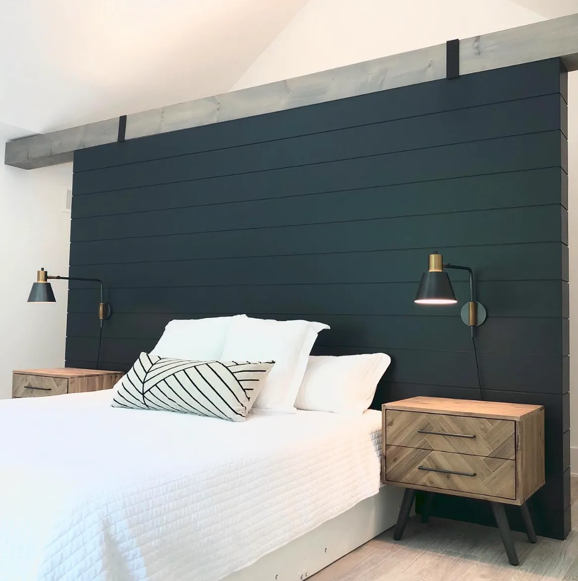 The deep navy shiplap wall in this bedroom exudes modern elegance. Paired with natural wood nightstands and sleek brass sconces, it’s a beautiful combination of contemporary and rustic. Shiplap is a versatile choice that you can install yourself if you’re handy with basic tools. It takes about a day to cut and attach the boards, followed by a day for painting and finishing touches. This bold, dramatic backdrop transforms the room into a stylish retreat.