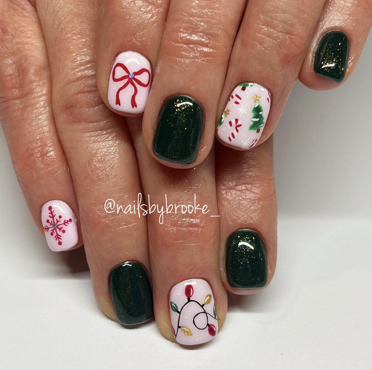 Mix & Match Christmas: A combination of deep green, bows, lights, and snowflakes on each nail brings variety and fun to this holiday manicure. It’s the perfect choice for anyone wanting a playful, vibrant holiday nail look. @nailsbybrooke___