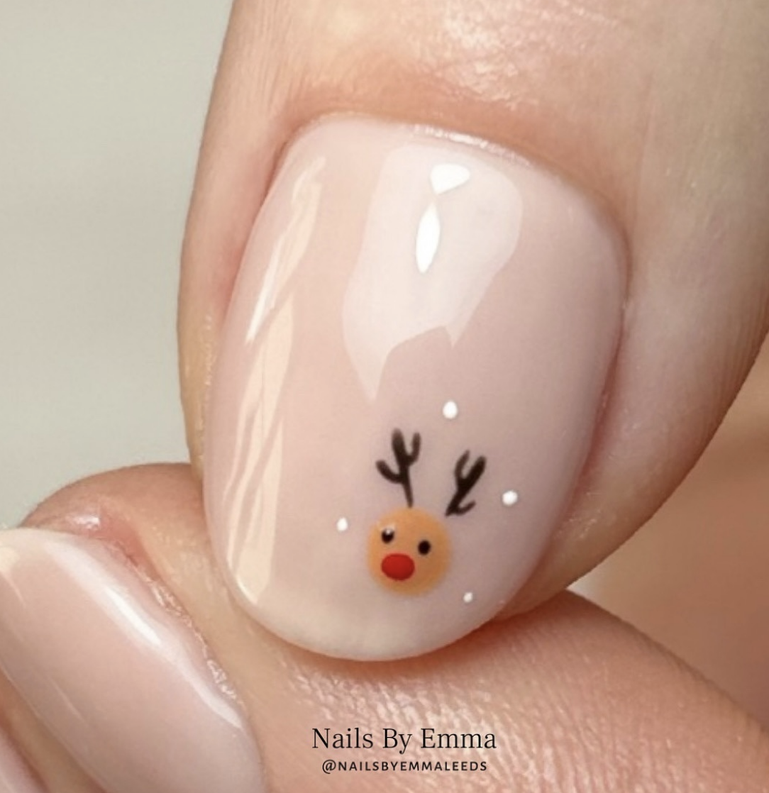 Minimal Rudolph: A simple nude base highlights a single reindeer design on an accent nail, complete with adorable antlers and a red nose. This understated design is ideal for a touch of festive cheer without going overboard. @naiksbyemmaleeds