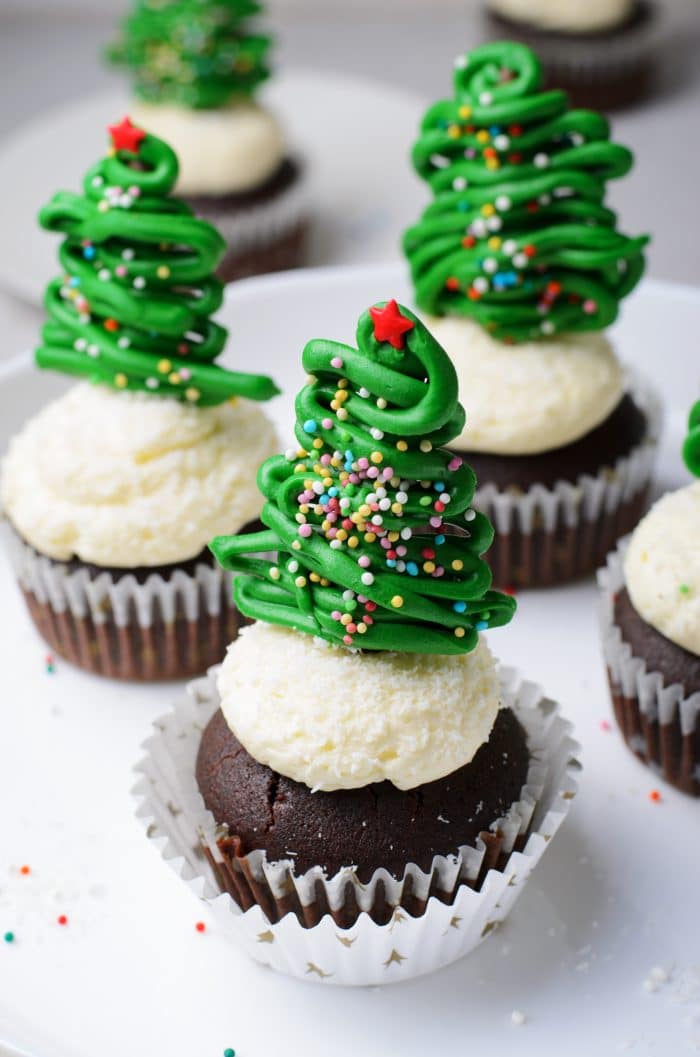 These cupcakes are decorated with Christmas trees made of swirled green frosting and sprinkles. A festive and classic cupcake that will look great on any holiday table!