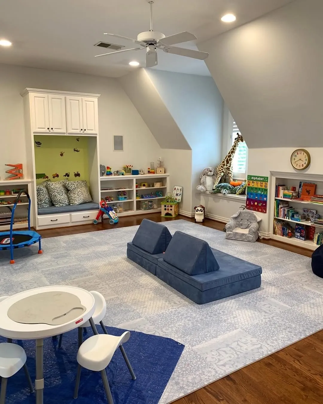 "Space to Play and Lounge" – A spacious room with activity zones for reading, jumping, and playing. The soft blue couch doubles as a space for both lounging and creative fort-building!