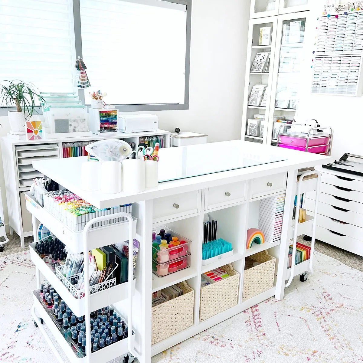 This bright and airy craft room features a spacious worktable with built-in cubbies and rolling carts—perfect for keeping essentials close while crafting!