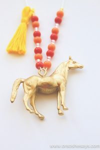 Gold painted horse charm hanging at the end of a beaded necklace complete with a tassel