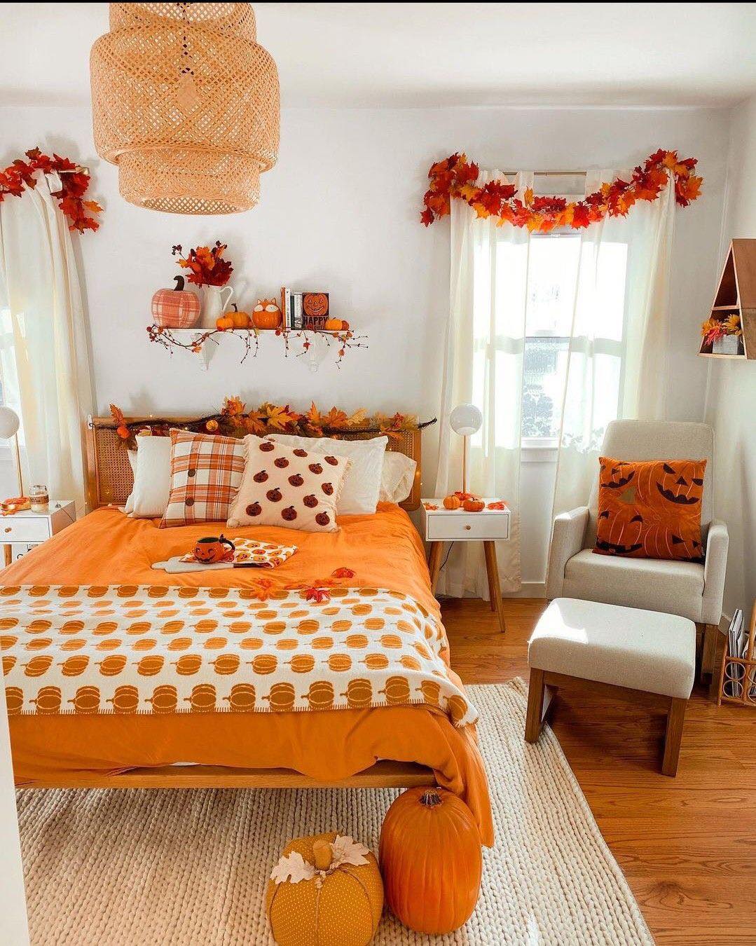 This bedroom is bursting with vibrant fall colors, creating a cheerful and cozy space that fully embraces the season. The bed is dressed in a bright orange duvet, paired with a playful pumpkin-themed throw and pillows in a mix of plaid and embroidered designs, adding layers of texture and warmth. Above the bed, a simple shelf displays a charming collection of small pumpkins and autumn decor, while garlands of red and orange leaves frame the windows, bringing the outdoors in. The corner chair is perfectly accented with a jack-o'-lantern pillow, tying the entire room together. From the woven rug to the warm wood tones, every detail in this room exudes a festive, fall-ready atmosphere that’s both inviting and stylish.