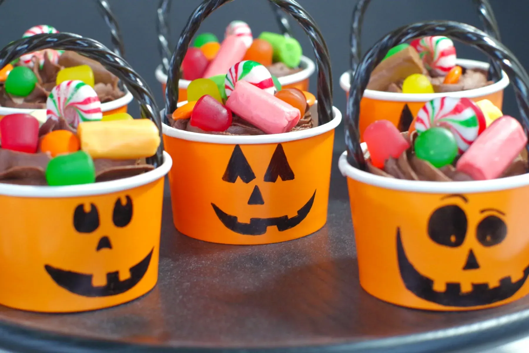 These cheerful cupcakes come in cute pumpkin-face cups and are topped with frosting and a mountain of colorful Halloween candyâsuper easy and perfect for little hands.