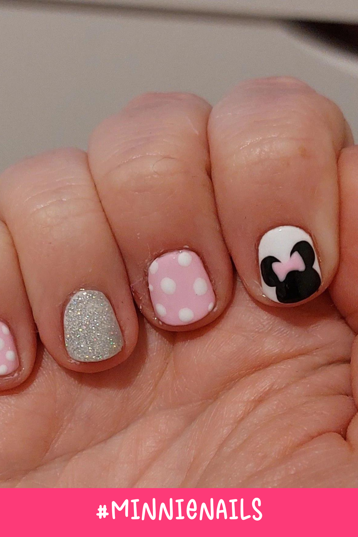 These Minnie Mouse nail designs feature a classic pink and white polka-dot pattern alongside a glittery silver accent. One nail showcases an adorable Minnie silhouette with a bow, making these easy Minnie Mouse nails perfect for Disney vacations.