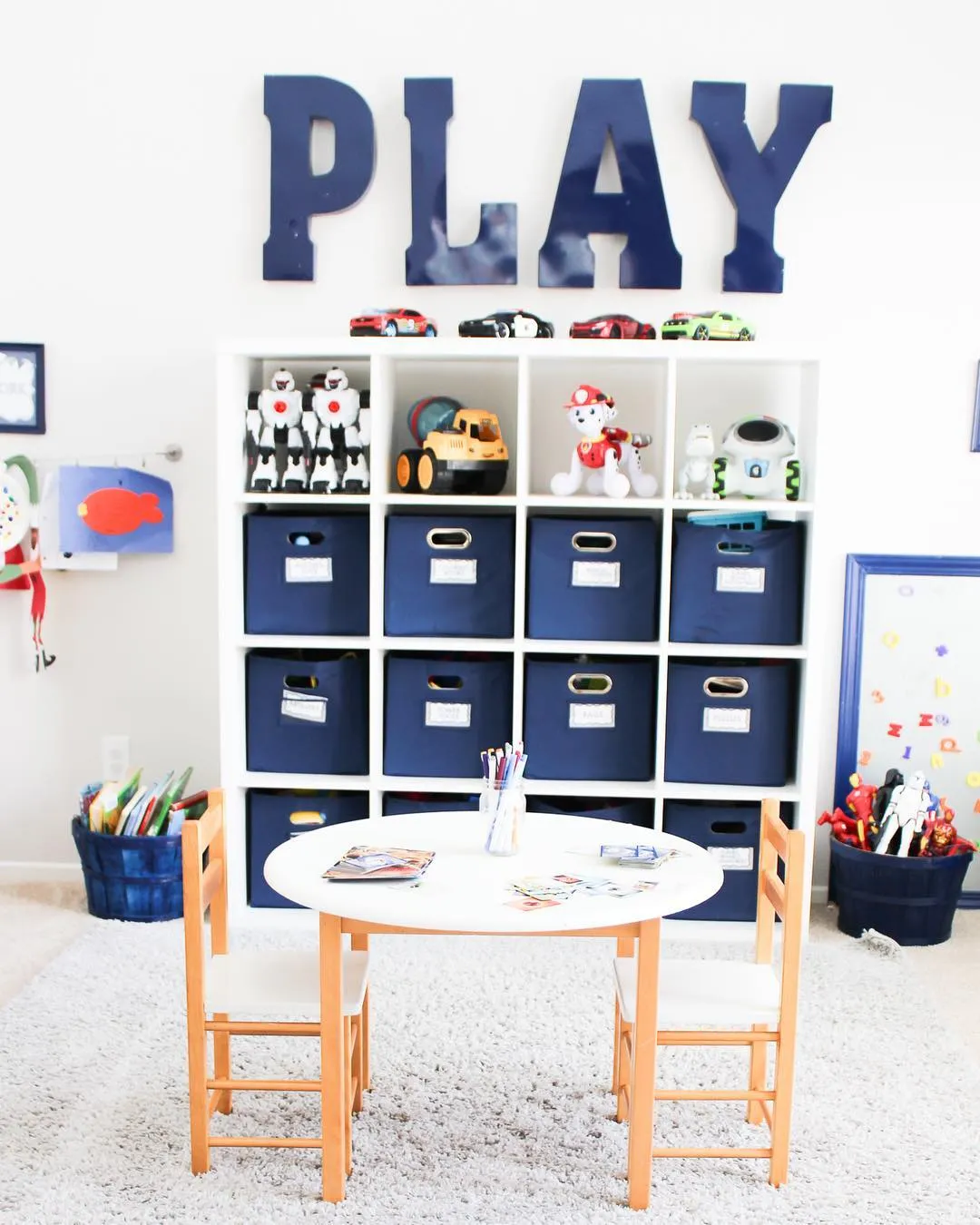 Classic Blue & White Playroom – A simple yet stylish setup with bold navy storage bins, oversized letters, and a practical layout for playtime and creativity.