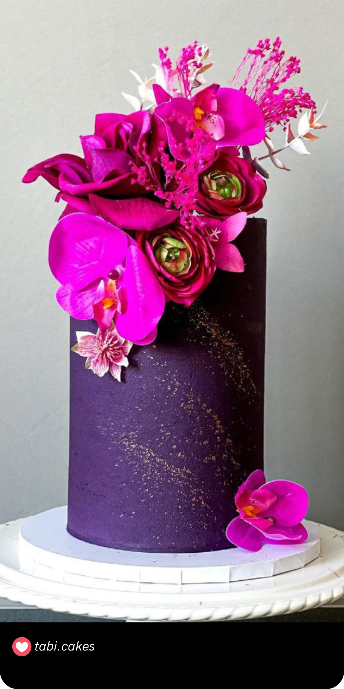 A sleek, modern cake with rich purple hues and a burst of magenta florals on top. The minimalist gold splatter adds just the right touch of glamour.