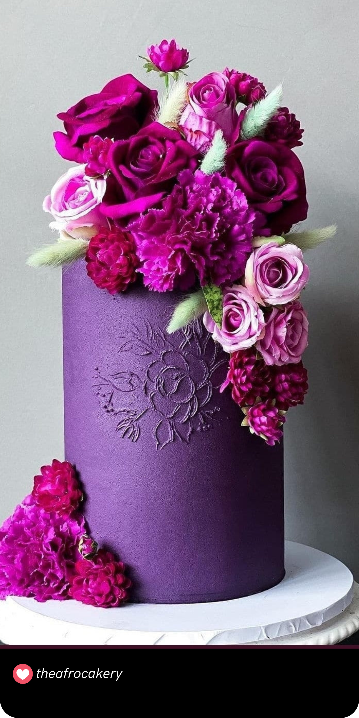 A sophisticated yet whimsical cake wrapped in a velvety purple finish and etched with floral designs. The clustered blooms in rich pinks and purples add a dramatic cascading effect.