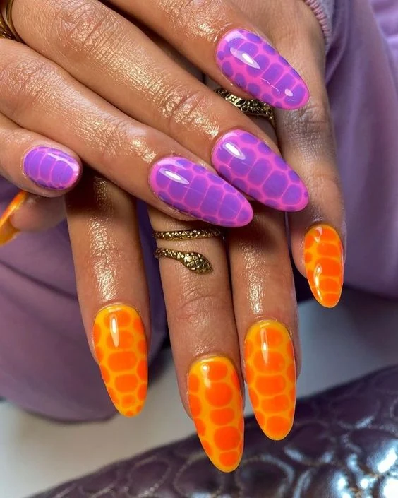 These nails feature a vibrant snake skin pattern with a glossy finish, alternating between a purple base with a pink scale overlay and an orange base with yellow scales. The design exudes a bold, exotic vibe perfect for making a statement.