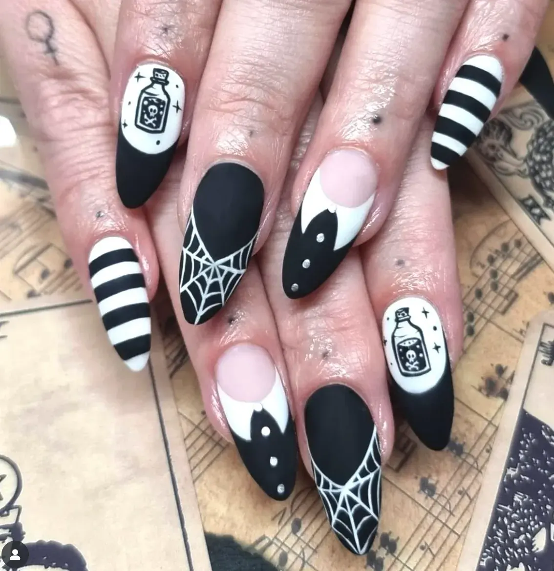 Matte black, striped accents, and tiny potion bottles give this look a witchy, gothic vibe. It’s Wednesday with a dash of mischief — the perfect Halloween manicure.