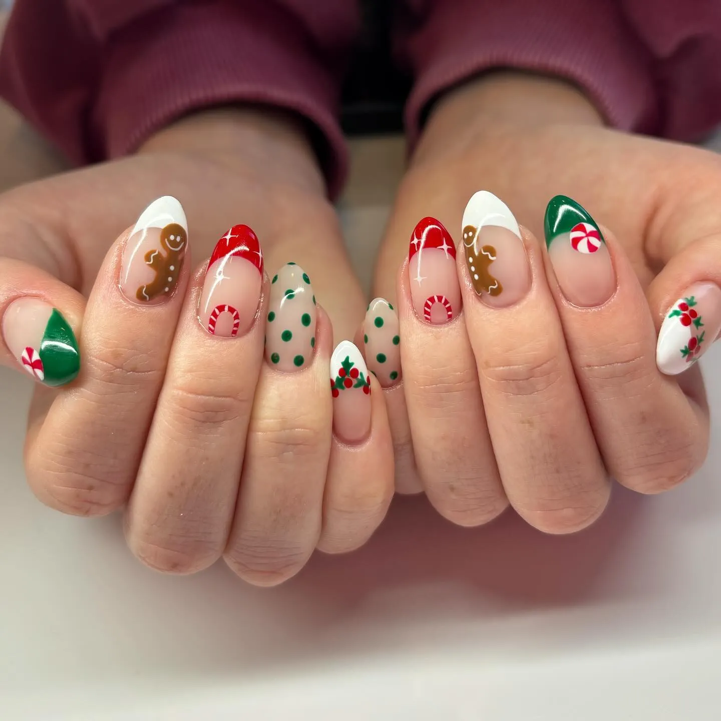 These red Christmas nails by @haileykaynails_ combine holly, gingerbread men, and candy details for a cute-meets-classic look. The almond shape keeps it elegant while still bringing tons of Christmas nail inspo.